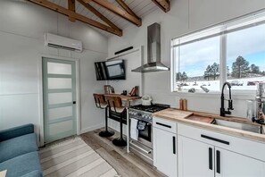 Una cocina moderna con armarios blancos, una estufa empotrada, un ventanal con vistas y un televisor montado sobre la encimera.