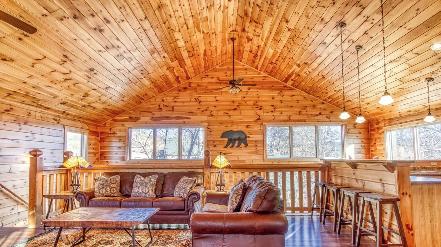 A log cabin interior with a high ceiling, wooden walls, a sofa, a table, and a bear decoration.