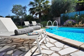 Ein Poolbereich mit Liegestühlen, einem Terrassenboden aus Steinplatten und einem klaren, blauen Pool.