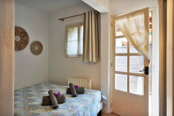 Ein Schlafzimmer mit einem Bett, einem Fenster mit Vorhängen, einem Heizkörper und zwei Wanddekorationen.