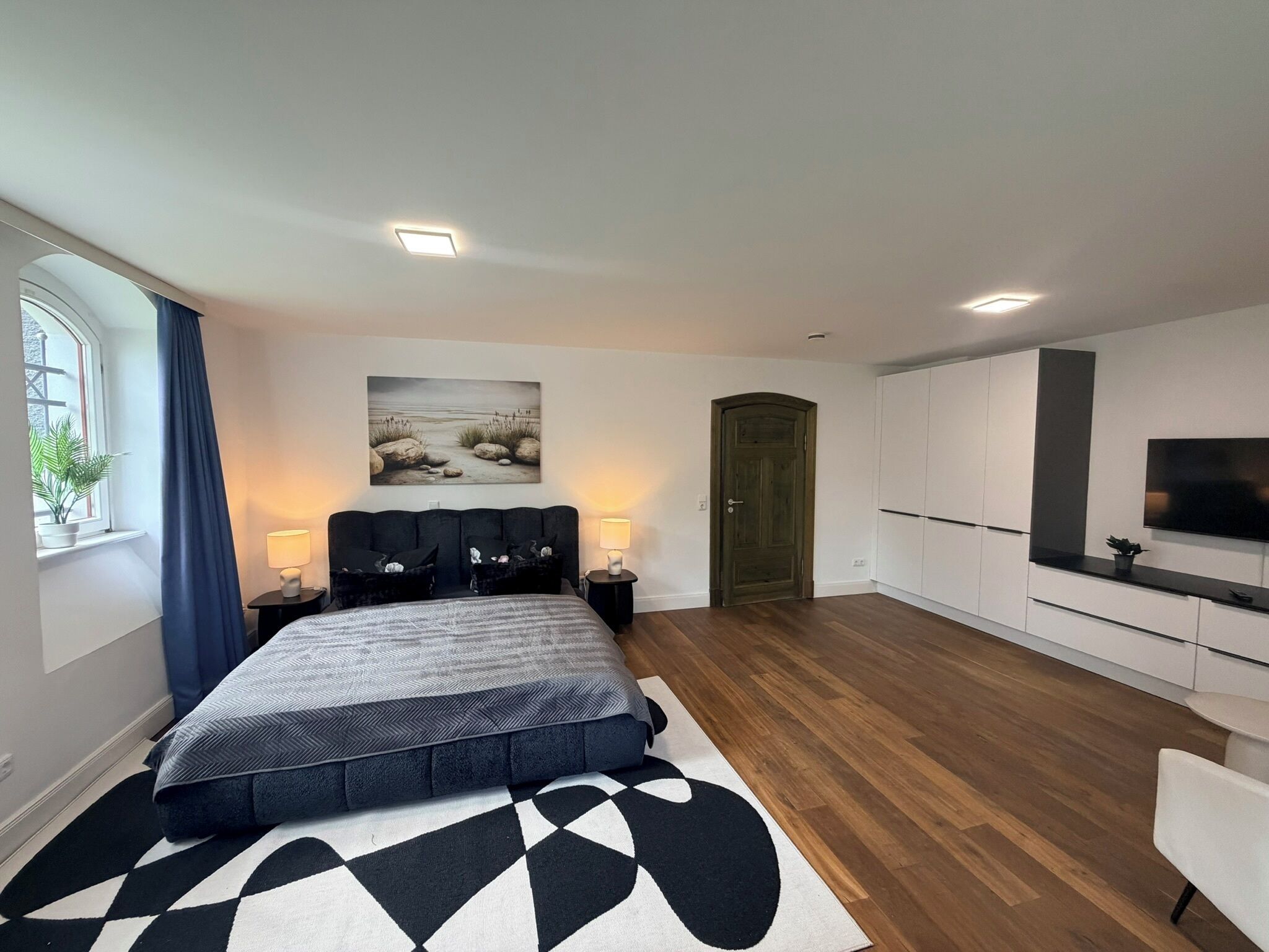 Un dormitorio moderno con cama, lámparas de noche, un cuadro, un armario y un televisor.