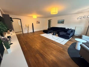 Ein modernes Wohnzimmer mit einem Ecksofa, einem runden Couchtisch, einem weißen Teppich und einem kleinen Beistelltisch.