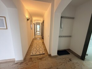 Un pasillo con un tapete estampado, un cuadro enmarcado a la izquierda y una puerta a la derecha.