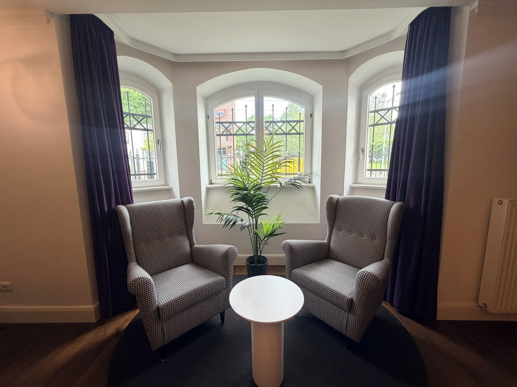 Ein Zimmer mit zwei Sesseln, einem kleinen runden Tisch und einer Topfpflanze.