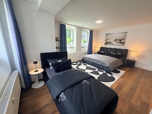 Un dormitorio moderno con cama, mesitas de noche, una lámpara y un ventanal con cortinas.