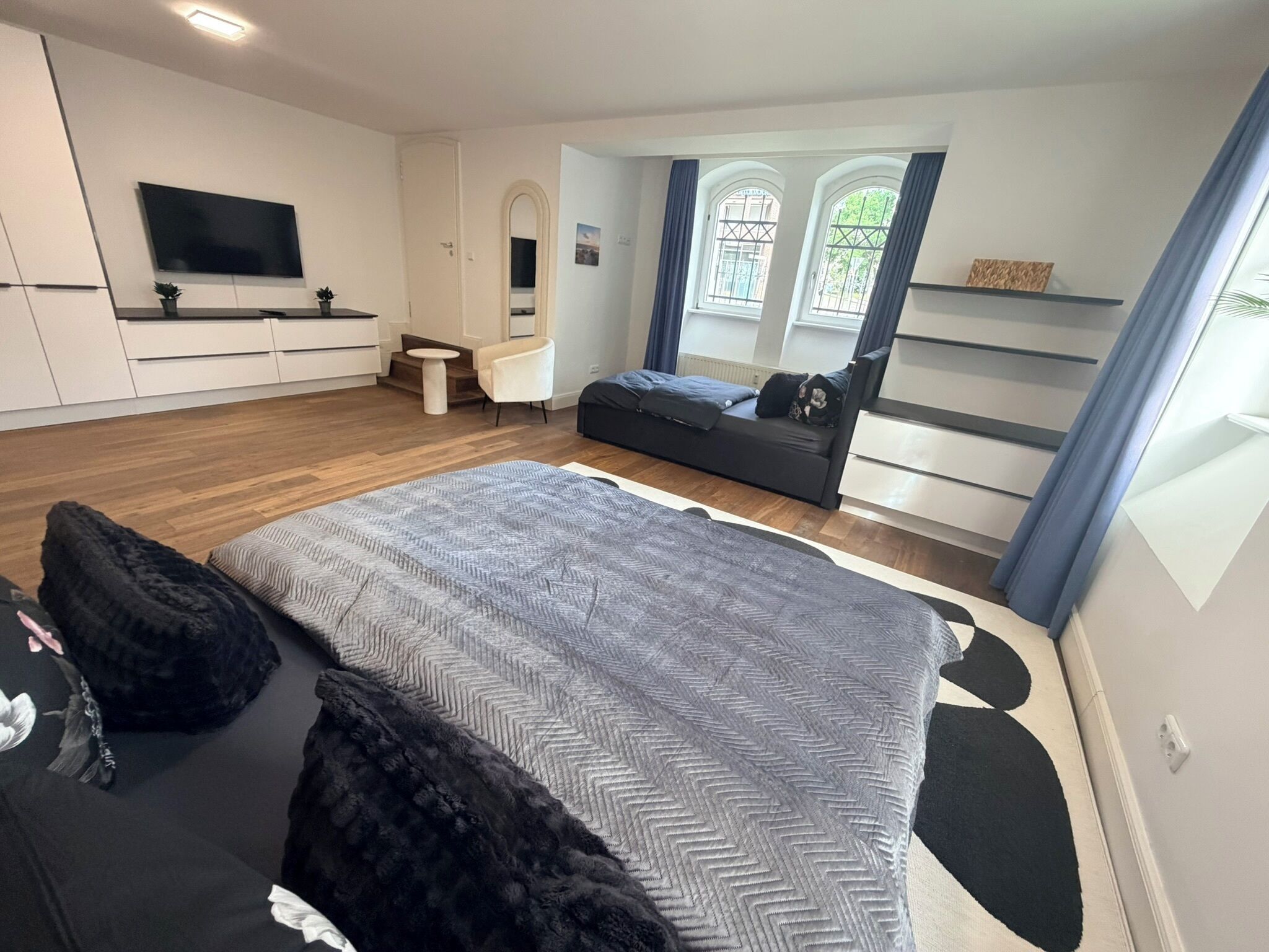 Een moderne slaapkamer met een groot bed, een televisie, een zithoek en een raam met gordijnen.