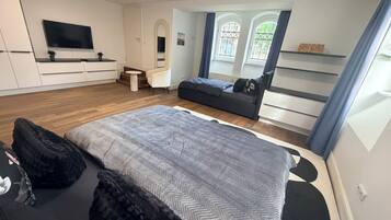 Een moderne slaapkamer met een groot bed, een televisie, een zithoek en een raam met gordijnen.