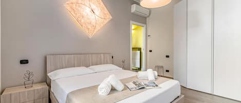 Una habitación de hotel moderna con una cama grande, mesitas de noche, una lámpara fijada a la pared y un armario.