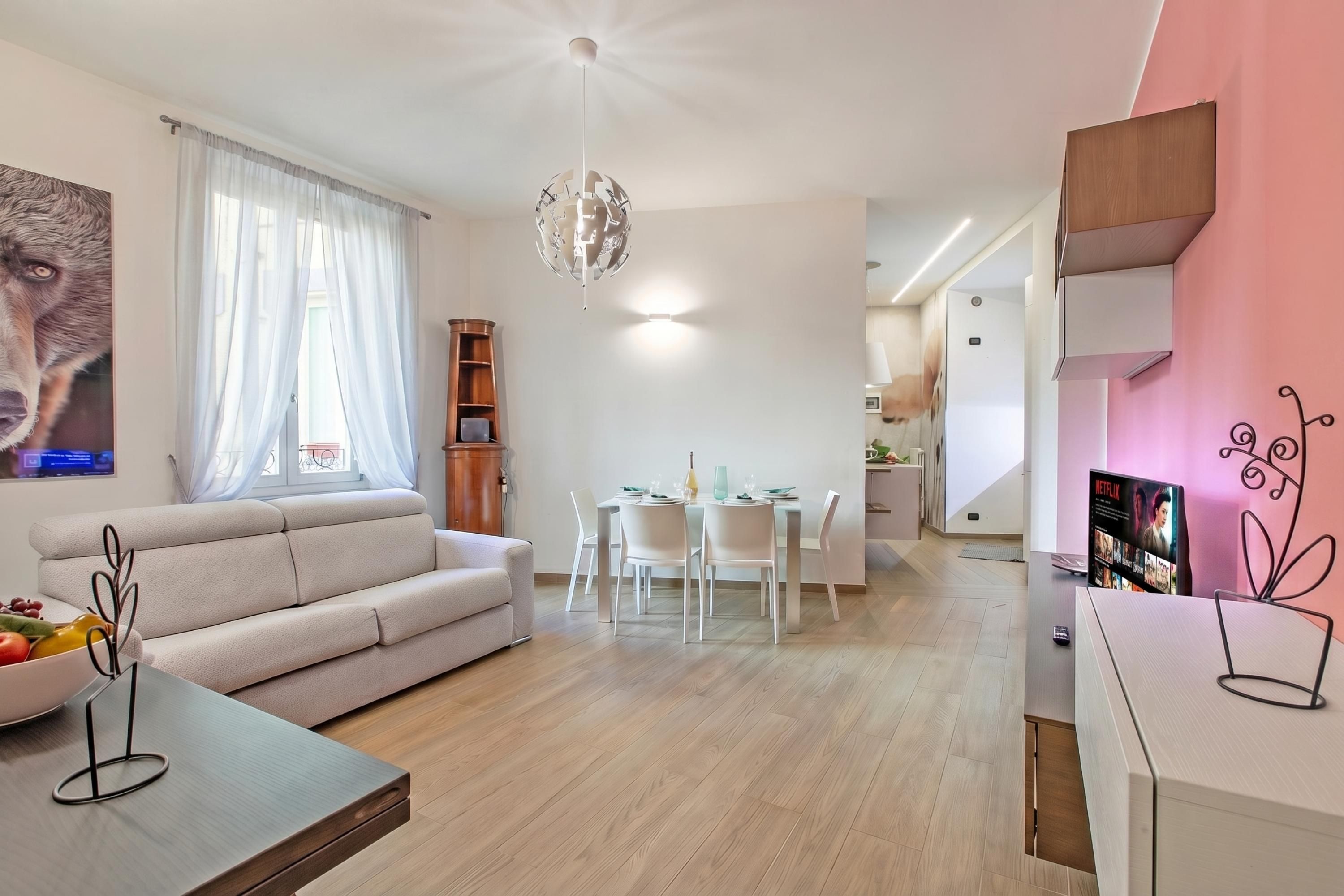 Ein modernes Wohnzimmer mit einer Couch, Esstisch und Stühlen, einer Pendelleuchte sowie einem Fernseher an der Wand.