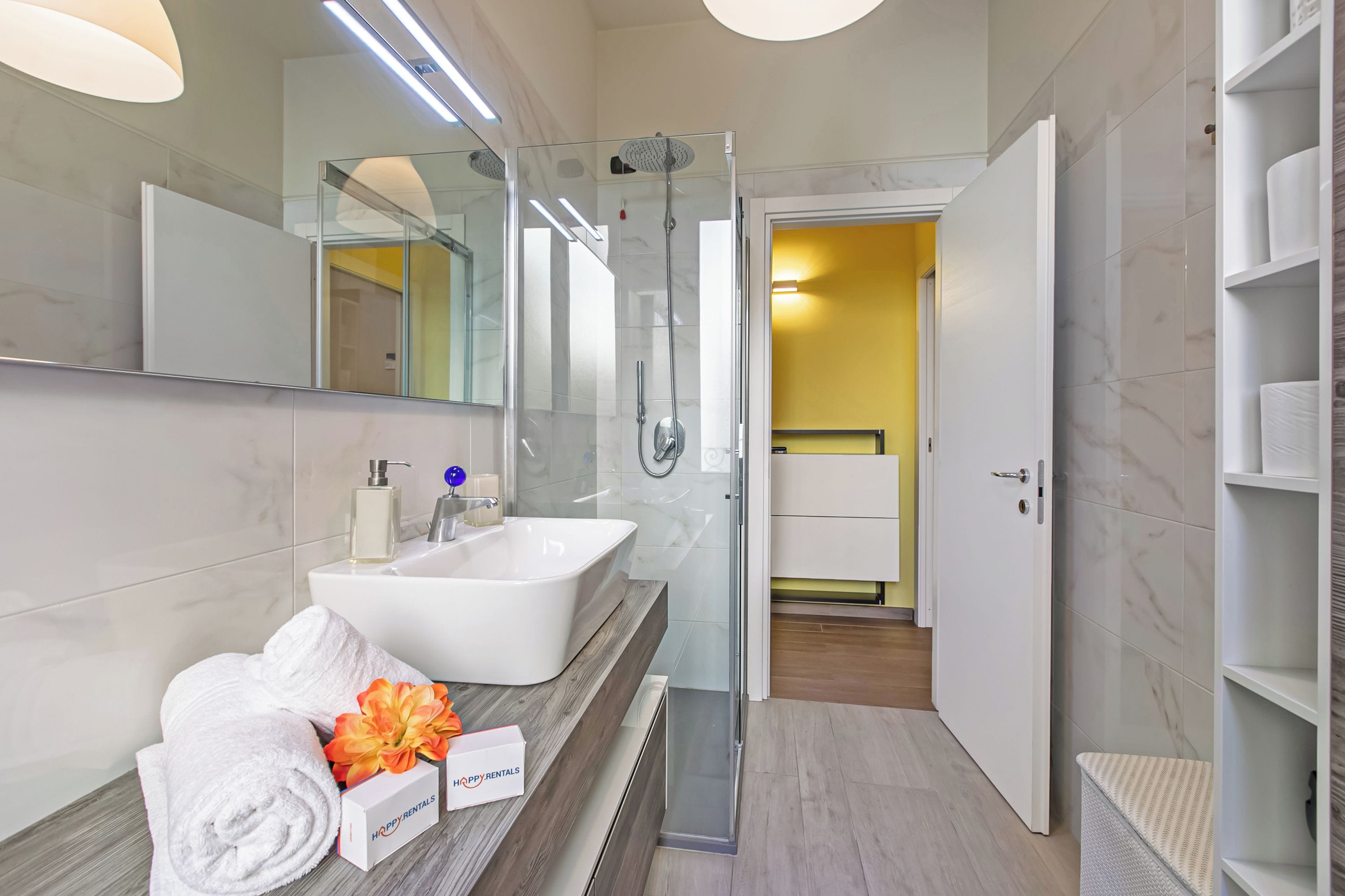 A modern bathroom with a glass shower enclosure, a white sink, and a vanity with towels and toiletries.