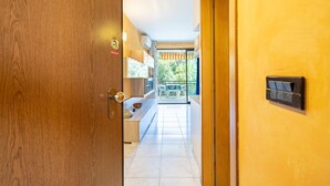 Hotelkamer met een houten deur, een klein tafeltje met stoelen, een balkon met uitzicht op groen en een betegelde vloer.