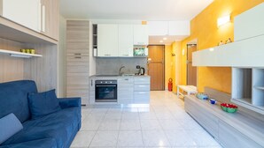 Een moderne keuken met een inbouwoven en magnetron, een blauwe bank en een eethoek met een lange bank.