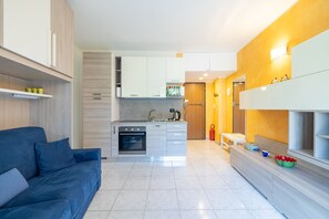 Eine moderne Küche mit Einbauofen und Mikrowelle, ein blaues Sofa sowie ein Essbereich mit einer Bank.