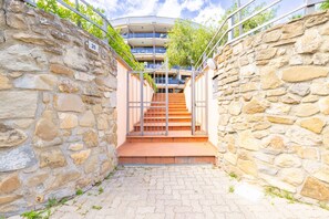 Ein mit Steinwänden ausgekleidter Gang, der zu einem mehrstöckigen Gebäude mit Treppe und Metallgeländern führt.