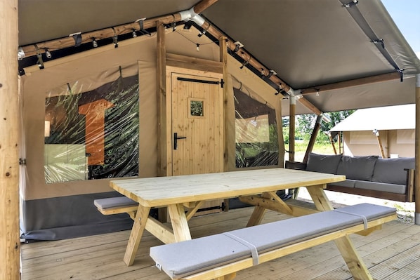 A wooden table and bench under a tent with a door and windows.