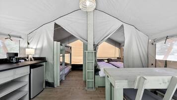 A tent with bunk beds, a desk with a lamp, and a small kitchenette.
