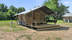 A small, single-story wooden structure with a covered porch and a picnic table. - Safari Tent Glamping with Riverside Relaxation Space in Blacksburg, Virginia (Blacksburg)