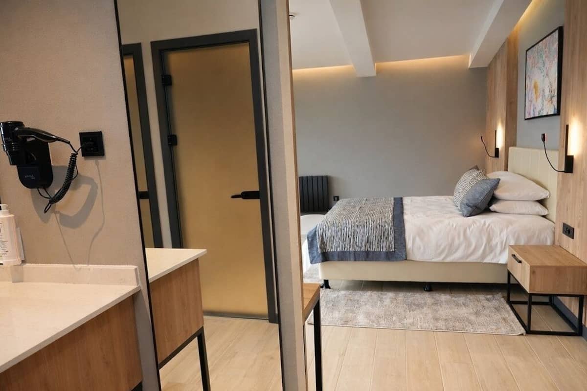 A modern hotel room with a bed, bedside table, and a desk with a chair.