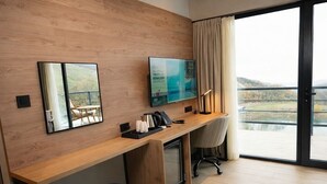 Ein modernes Hotelzimmer mit einem Holztisch, einem Flachbildfernseher, einem Sessel und Blick auf ein Gewässer durch ein großes Fenster.