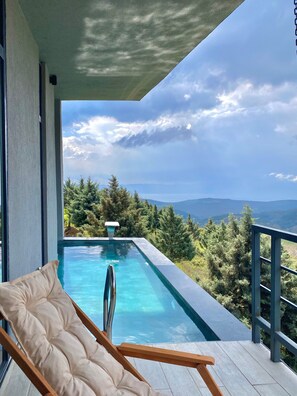 A balcony with a pool, a lounge chair, and a view of the mountains.