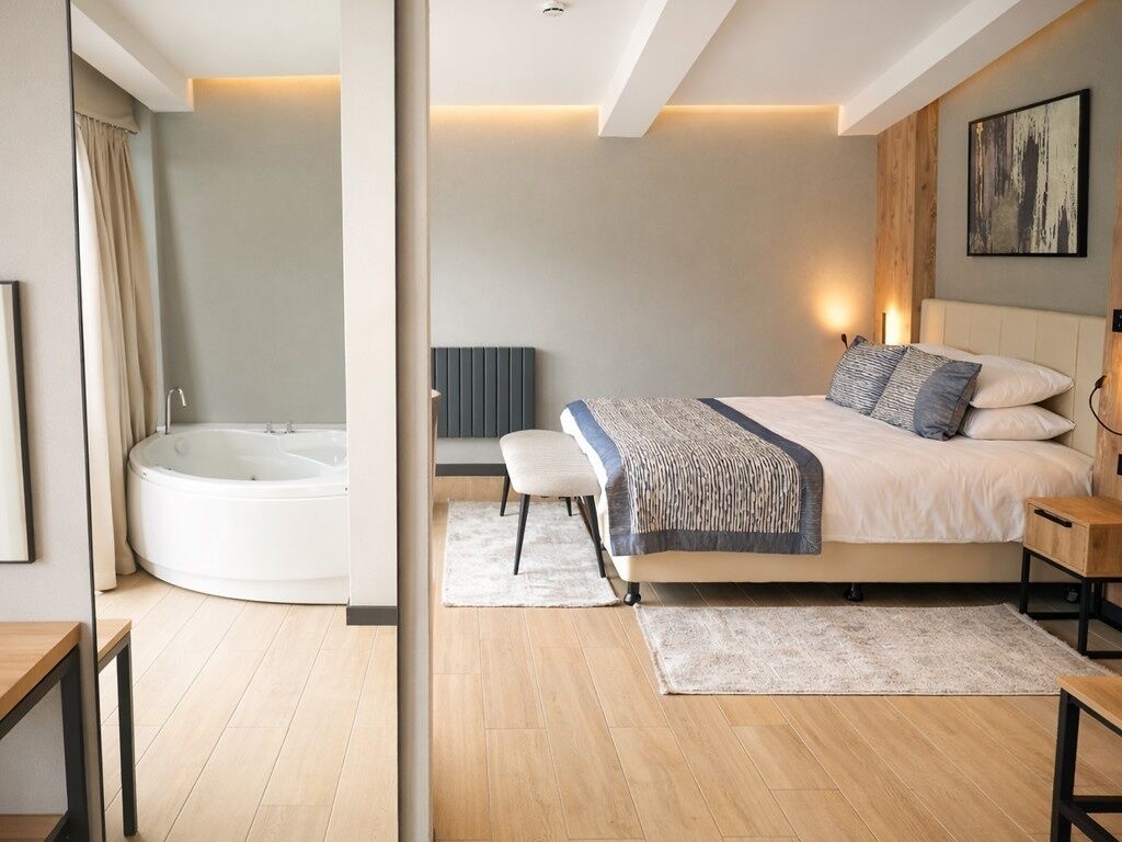 Un dormitorio moderno con una cama grande, una mesita de noche, una lámpara auxiliar, una obra de arte en la pared y una bañera empotrada.