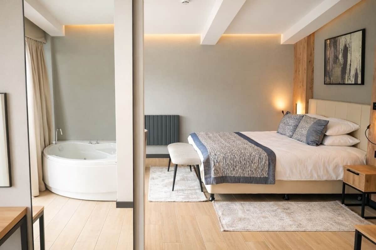 A modern bedroom with a large bed, a bedside table, a nightstand, a wall-mounted artwork, and a built-in bathtub.