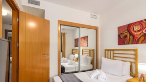 Une chambre d’hôtel avec une armoire en bois, un lit avec du linge de maison blanc, une table de chevet avec une lampe et un tableau au mur.
