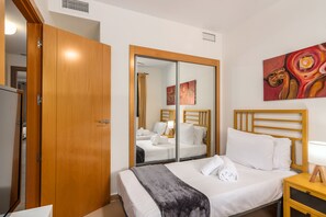 Habitació d'hotel amb armari de fusta, llit amb roba blanca, tauleta de nit amb làmpada i un quadre a la paret.