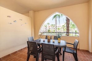 A dining area with a table and chairs, a window with a view of palm trees and buildings, and wall decorations. - Playa Marina - Punta del Moral Beach PPHM208P32 (Punta del Moral)