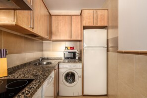 A compact kitchen with wooden cabinets, a microwave, a refrigerator, a washing machine, and a sink. - Playa Marina - Punta del Moral Beach PPHM208P32 (Punta del Moral)