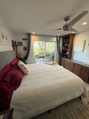 Ein Schlafzimmer mit Bett, Deckenventilator, Blick durch eine Glastür und einem Holzschrank.