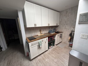 Une cuisine compacte avec des meubles blancs, un plan de travail en bois et un four à micro-ondes encastré.
