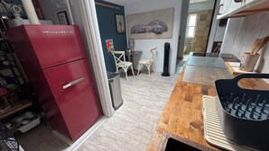 A compact kitchen with a red refrigerator, a wooden dining table, and a black kettle.