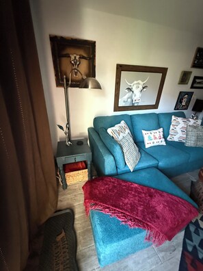 Un salon avec un canapé de couleur turquoise, un plaid rouge, une lampe et des œuvres d’art accrochées au mur.