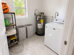 Ein Waschraum mit Waschmaschine, Warmwasserbereiter und Aufbewahrungsboxen.