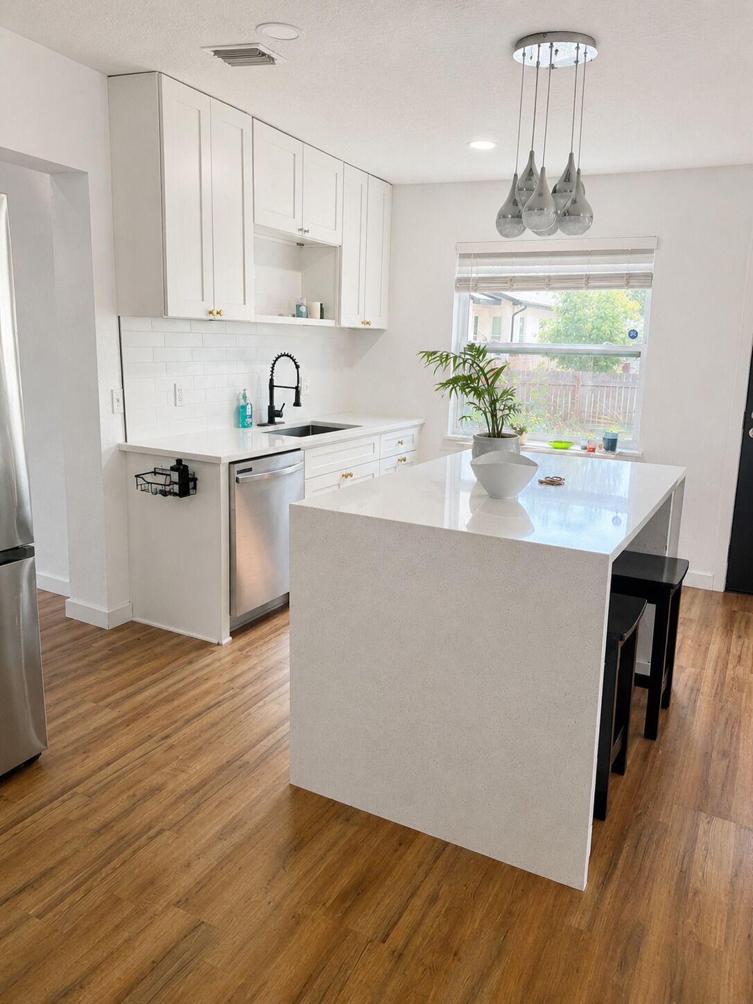 A modern kitchen with white cabinetry, a central island, and a window providing a view of the outdoors.