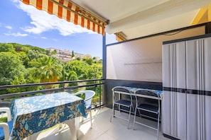 Ein Balkon mit Tisch und Stühlen, einem Kühlschrank und Blick auf eine grüne Hügellandschaft mit Gebäuden.