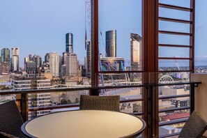 Ein Balkon mit Tisch und Stühlen, der auf einen Stadtblick mit modernen Gebäuden und einem Riesenrad blickt.