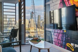 A modern room with a large window, a glass table with books, a chair, and a colorful mural. - Urban Escape: Great location w/ Brisbane Cityscape (South Brisbane)