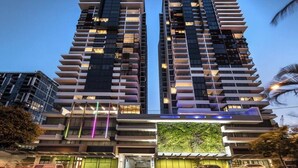 Un edificio de gran altura con varios balcones, una pared verde en la base y un cielo despejado.