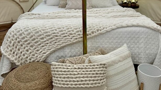 A tented room with a bed, pillows, a woven basket, and a small table.