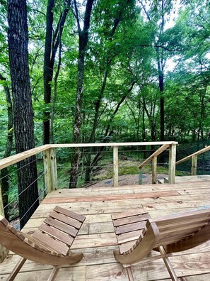 A wooden deck with two wooden benches and a railing, surrounded by a forest.