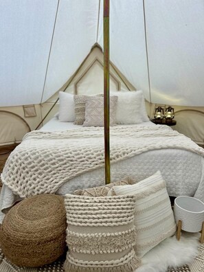 Una habitación con tienda de campaña, una cama, almohadas, una cesta tejida y una mesita.