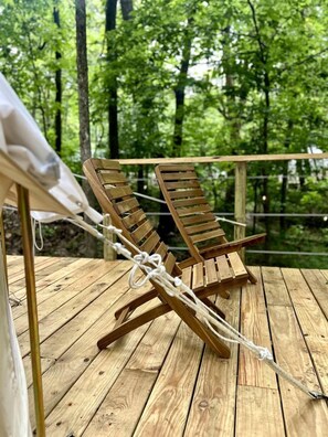 Two wooden lounge chairs on a wooden deck with a forest backdrop.