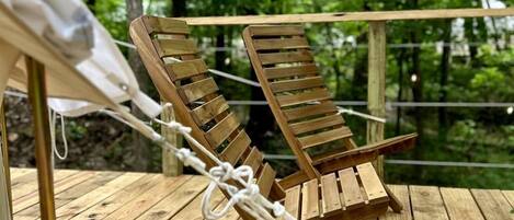 Dos sillones de madera en una terraza de madera con un bosque de fondo.