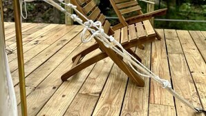Two wooden lounge chairs on a wooden deck with a forest backdrop.