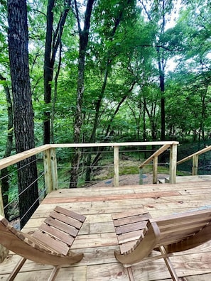 Eine Holzterrasse mit zwei Bänken und einem Geländer, umgeben von einem Wald.