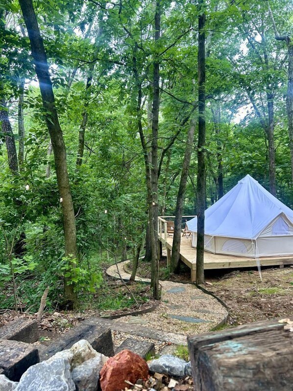 A tent in a forest with a wooden deck and a circular stone path.
