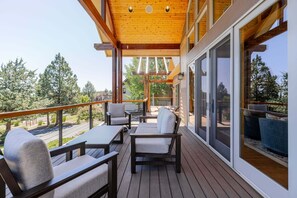 A wooden deck with outdoor furniture, large windows, and a view of trees. - Above The Crest - Views! Elegantly Perched, Hot Tub, Table Tennis, Luxury, Peaceful (Redmond)