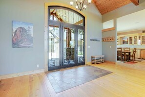 A spacious interior with a large wooden door, a dining area with chairs, and a kitchen visible through an archway.